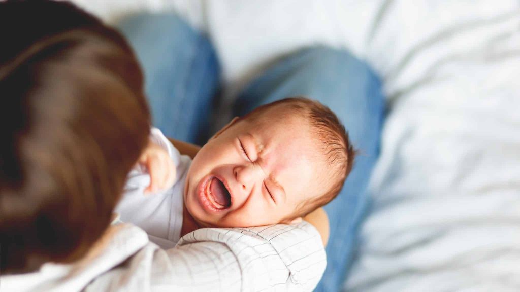 Un bébé pleure dans les bras d'un adulte