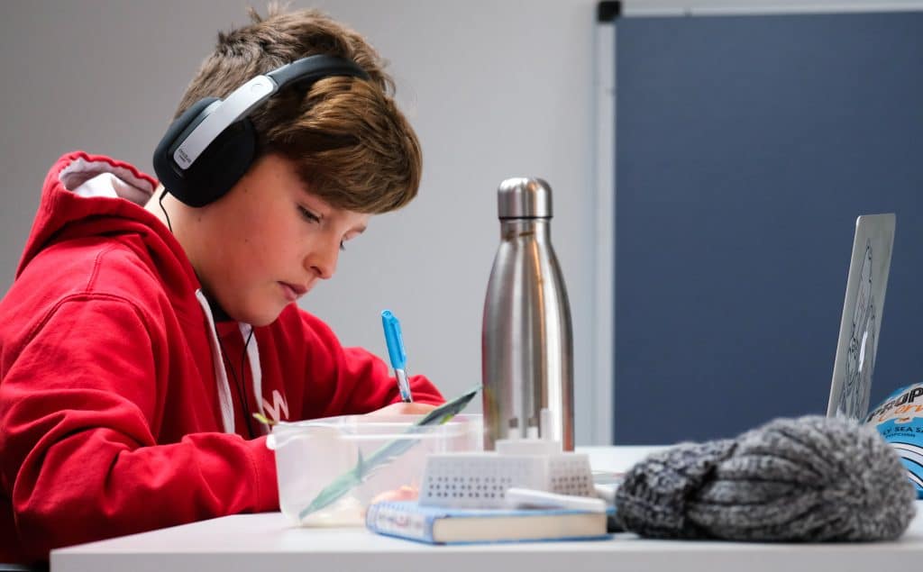 Un jeune homme fait ses devoirs avec un casque sur les oreilles.