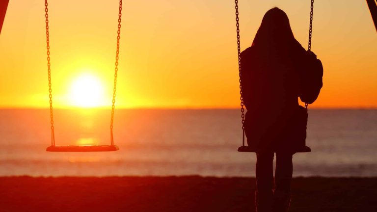 femme de dos, seul sur balaçoire, et autre balançoire vide regarde le couché du soleil