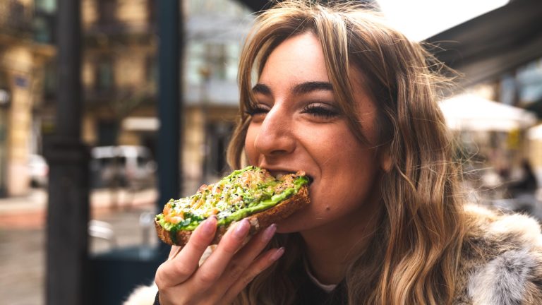 Une femme mange une tartine avec de l'avocat.