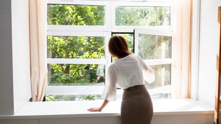 Une femme aère son logement. Prévention pollution de l'air intérieur.