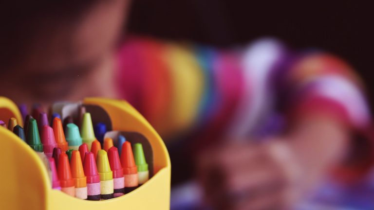 Des crayons de couleurs en premier plan en deuxième planun enfant dessine