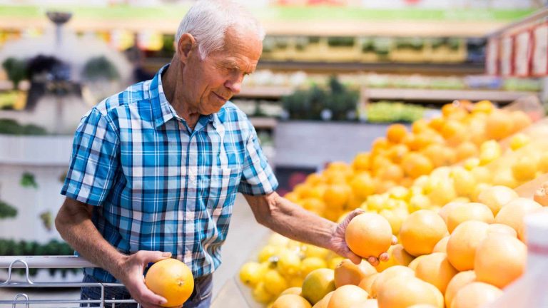 Un homme choisit son pamplemousse dans un supermarché.