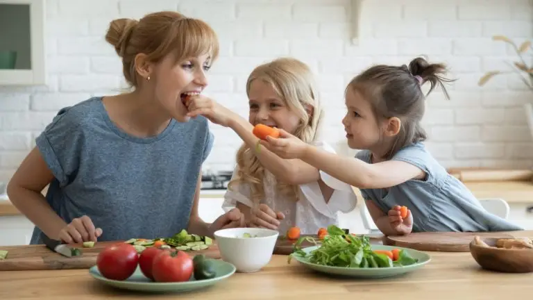 Une femmes avec deux petite dans une cuisine mangent des carottes.