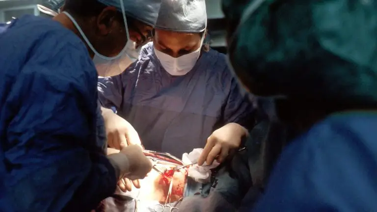 Biopsy. A Caucasian woman patient is being operated on. Her nipple is being incised by the surgeon. The male surgeon and an operating room attendant are visible. A surgical biopsy is being performed to determine exact nature of solid tumor.