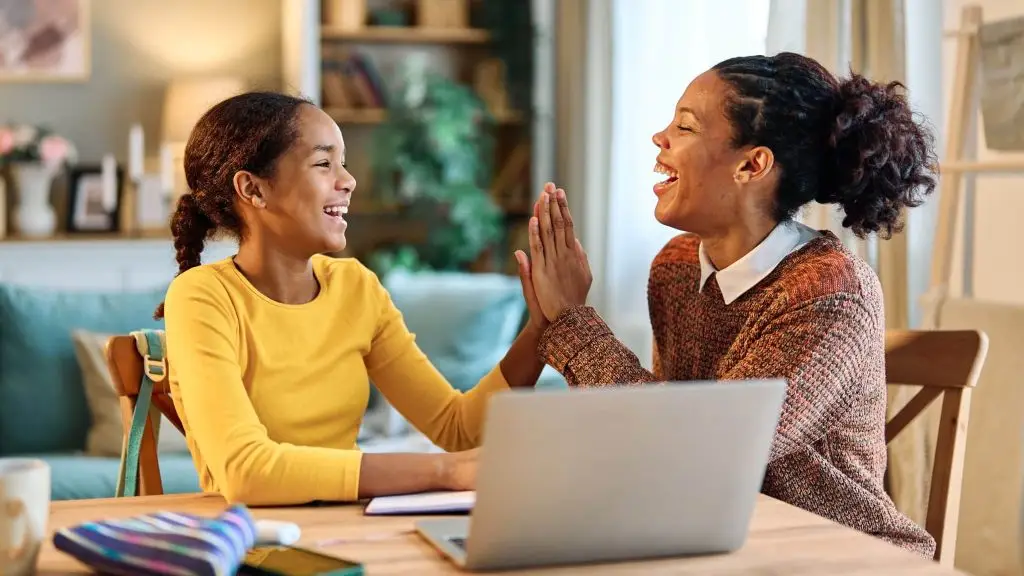 Une jeune fille et dame souriantes sont assises sur une table devant un écran d'ordinateur