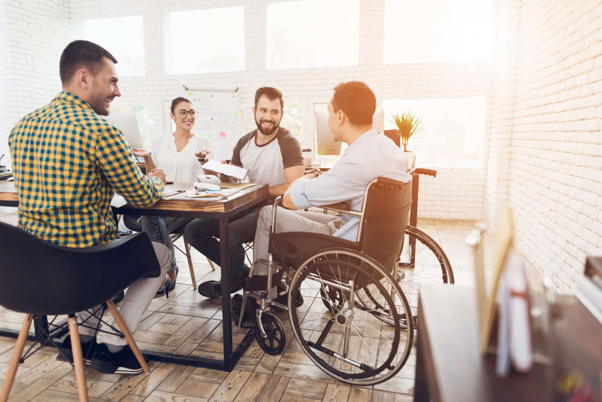 A man in a wheelchair communicates cheerfully with employees of the office during a business meeting.