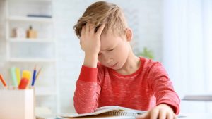 Un enfant qui fait ses devoirs met sa main sur tête parce qu'il a une migraine