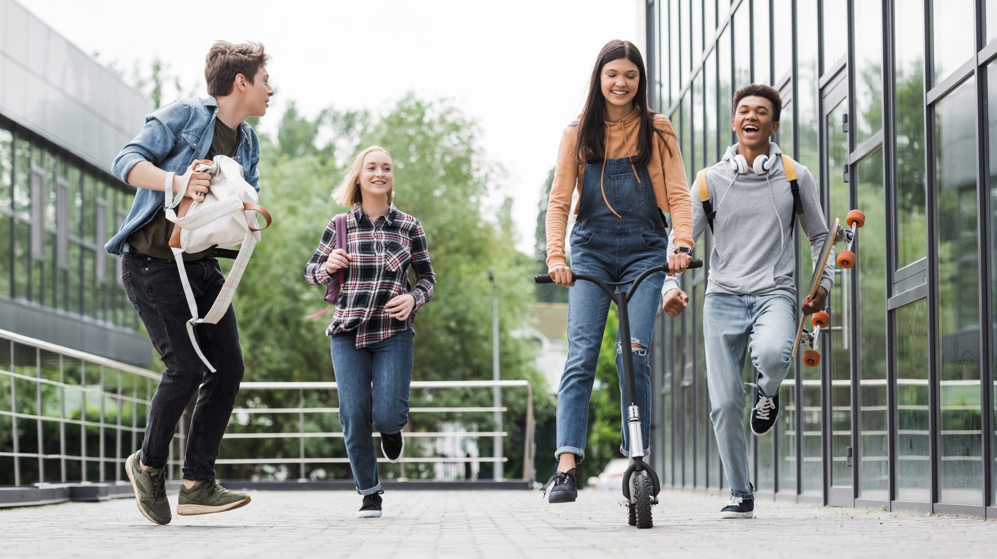 Quatre adolescents jouent en extérieur. Ils sont contents. L'une fait de la trottinette.