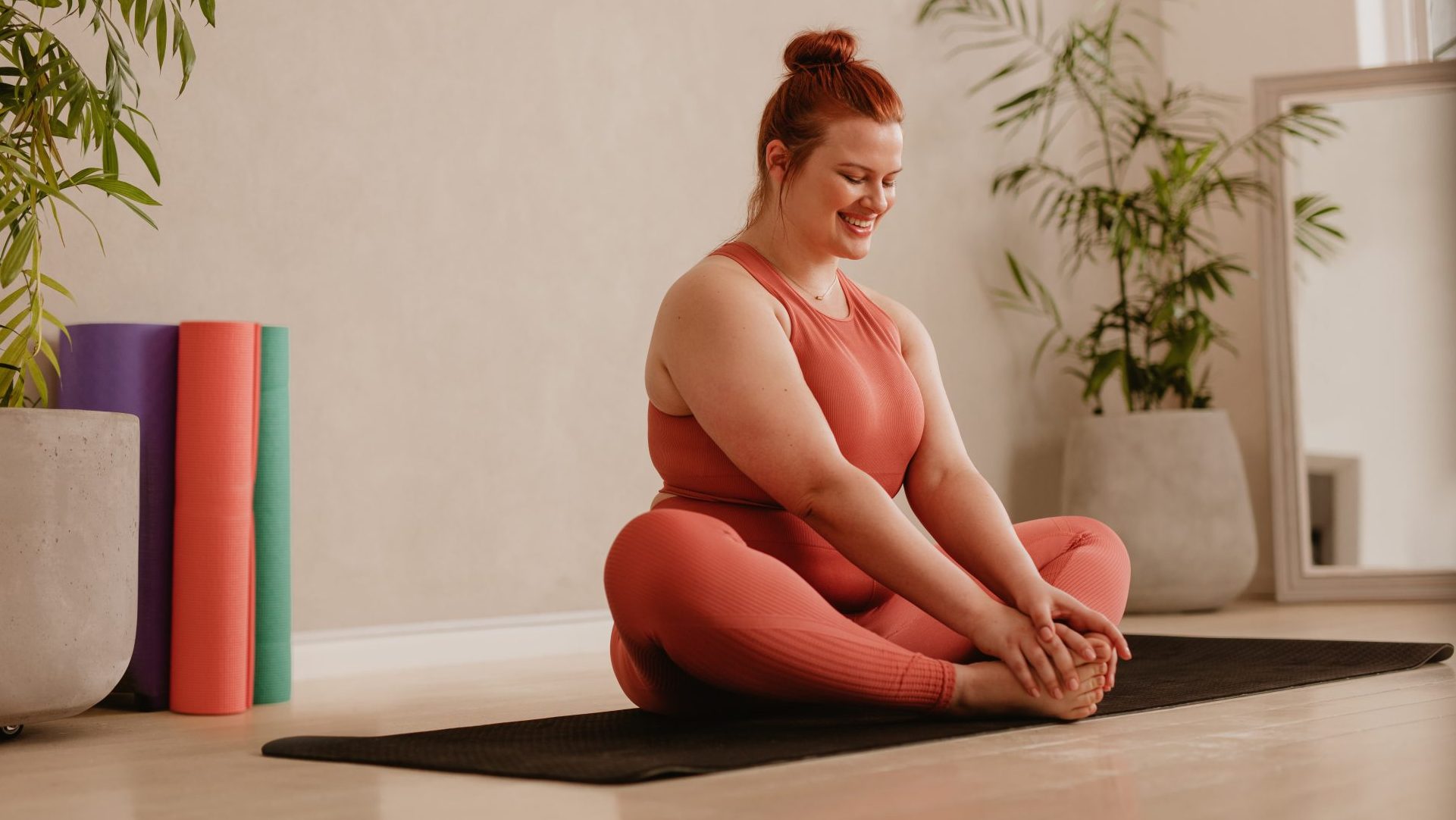 Une femme est assise sur un tapis de yoga. Elle sourit