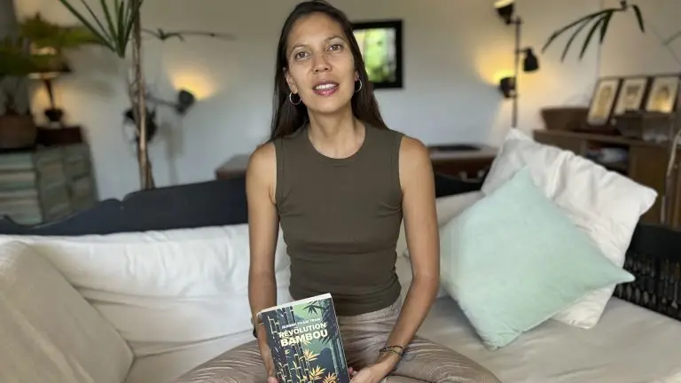 L'auteure Jeanne Pham Tran est assise dans son salon les jambes en tailleur. Elle tient dans sa main son livre "Révolution bambou".