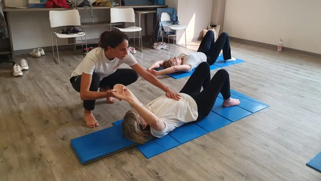 Lucie Mehats, praticienne en thérapie sportive a la CAMI Sport & Cancer, est accroupie auprès d'une participante qui est allongée au sol. Elle l'aide à accomplir un geste