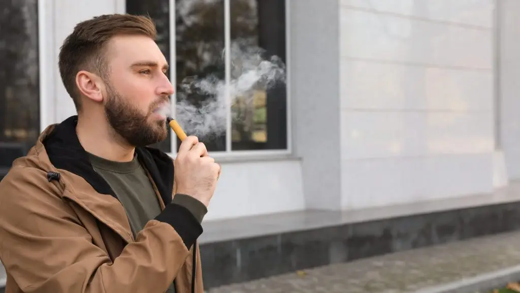 Un homme fume une cigarette électroniques jetable.