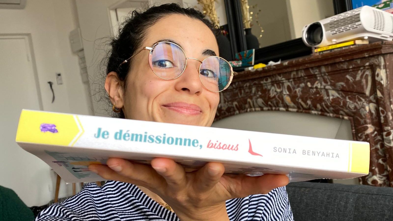 Sonia Benyahia tient son livre "Je démissionne, bisous". Elle porte de lunettes de vue et elle sourit.