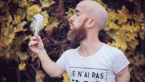 Un homme barbu de petite taille souffle sur une plume blanche