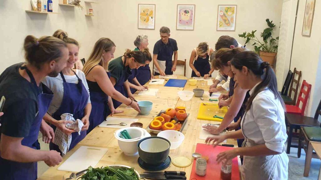 Un atelier culinaire est organisé. Il y a une dizaine de participants autour d'une table. Il porte un tablier bleu