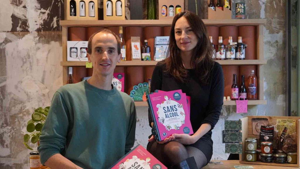 Augustin Laborde, fondateur de la cave sans alcool parisienne Le Paon qui Boit, et Maud Catté une des salariés, tiennent chacun dans leur main le livre "“Sans alcool : 1001 boissons pour un nouvel art de vivre”