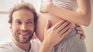 Père qui pose son oreille contre le ventre de sa femme enceinte.