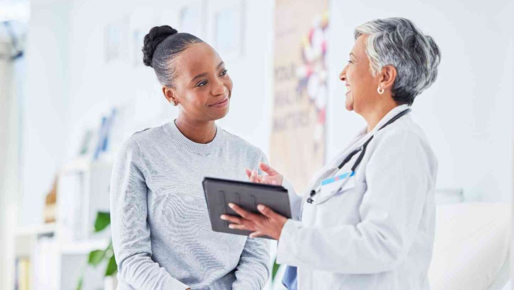 Une femme est assise sur une table d'examen devant elle il y a une femme médecin