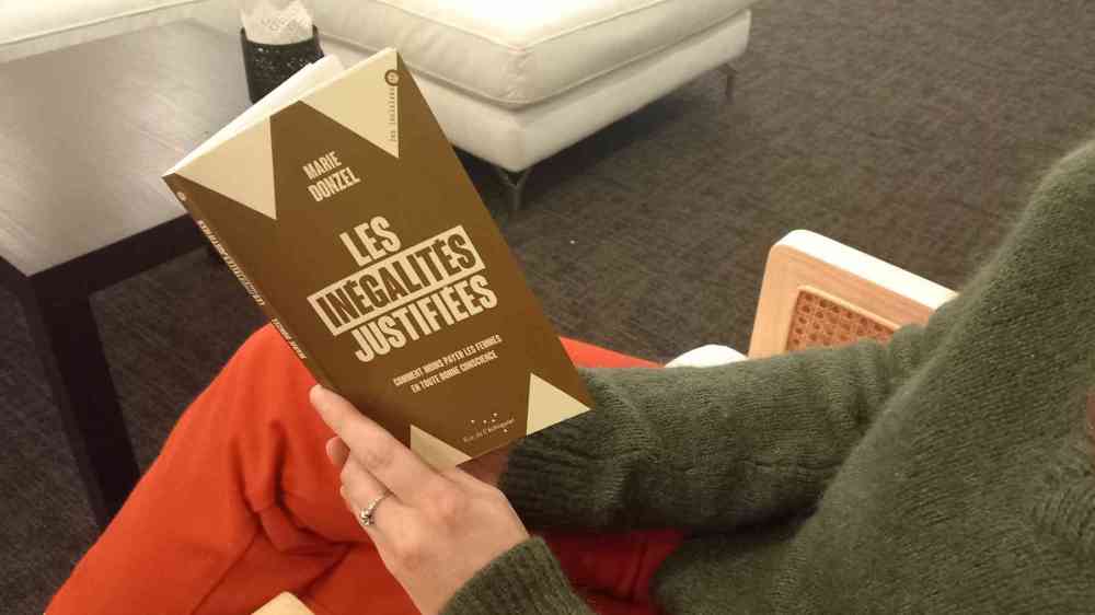 Livre : “Les inégalités justifiées”. Une personne est assise sur une chaise elle tient le livre de Marie Donzel