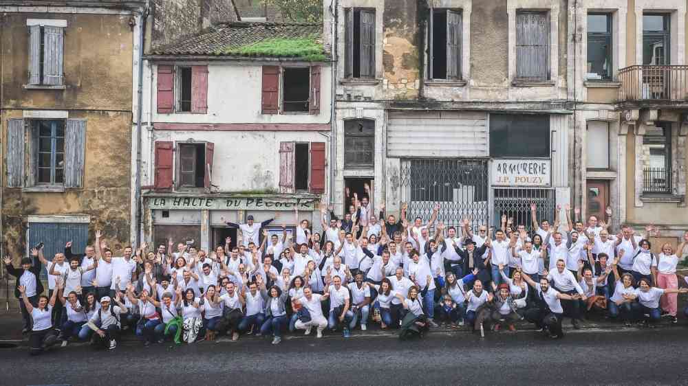 L'équipe d'investir ensemble pose dans la rue devant plusieurs habitations. Les gens portent un t-shirt blanc et ont l'air content.