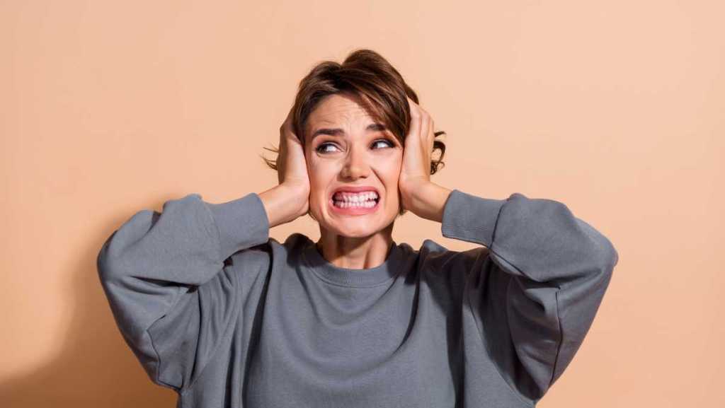 Santé auditive : quelles solutions pour limiter les nuisances sonores ? Une femme grimace. Elle met ses mains sur ses oreilles.